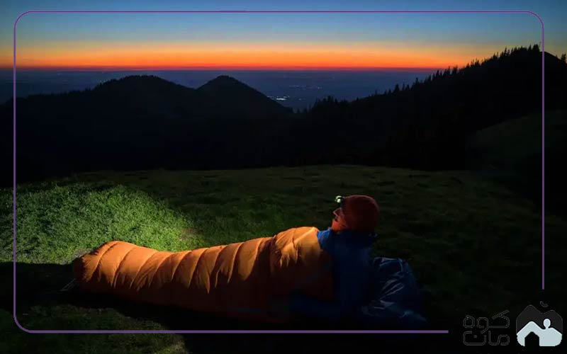 A climber sleeping in a sleeping bag with a headlamp on his head